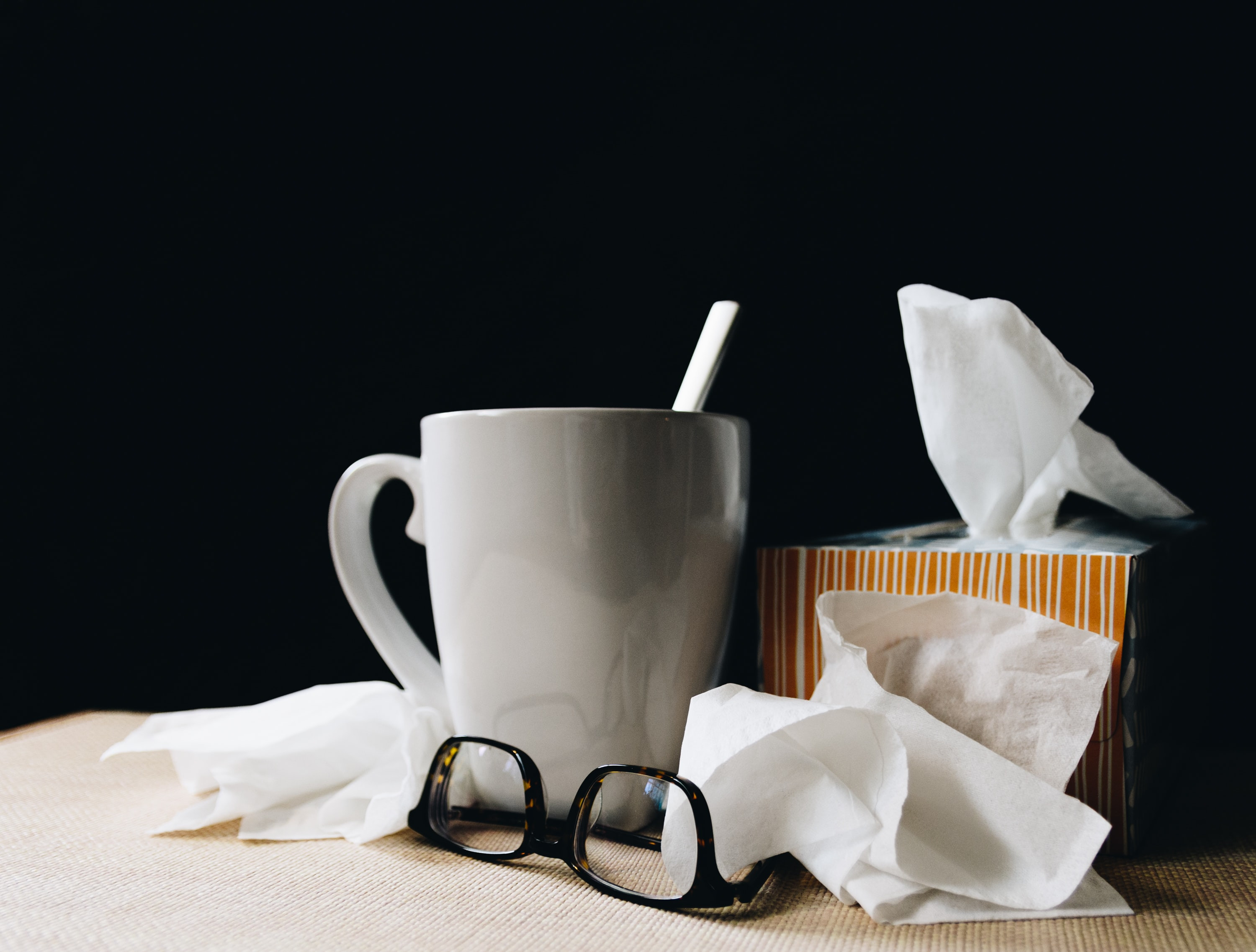 image of tissues, used tissues, a pair of glasses, and a mug