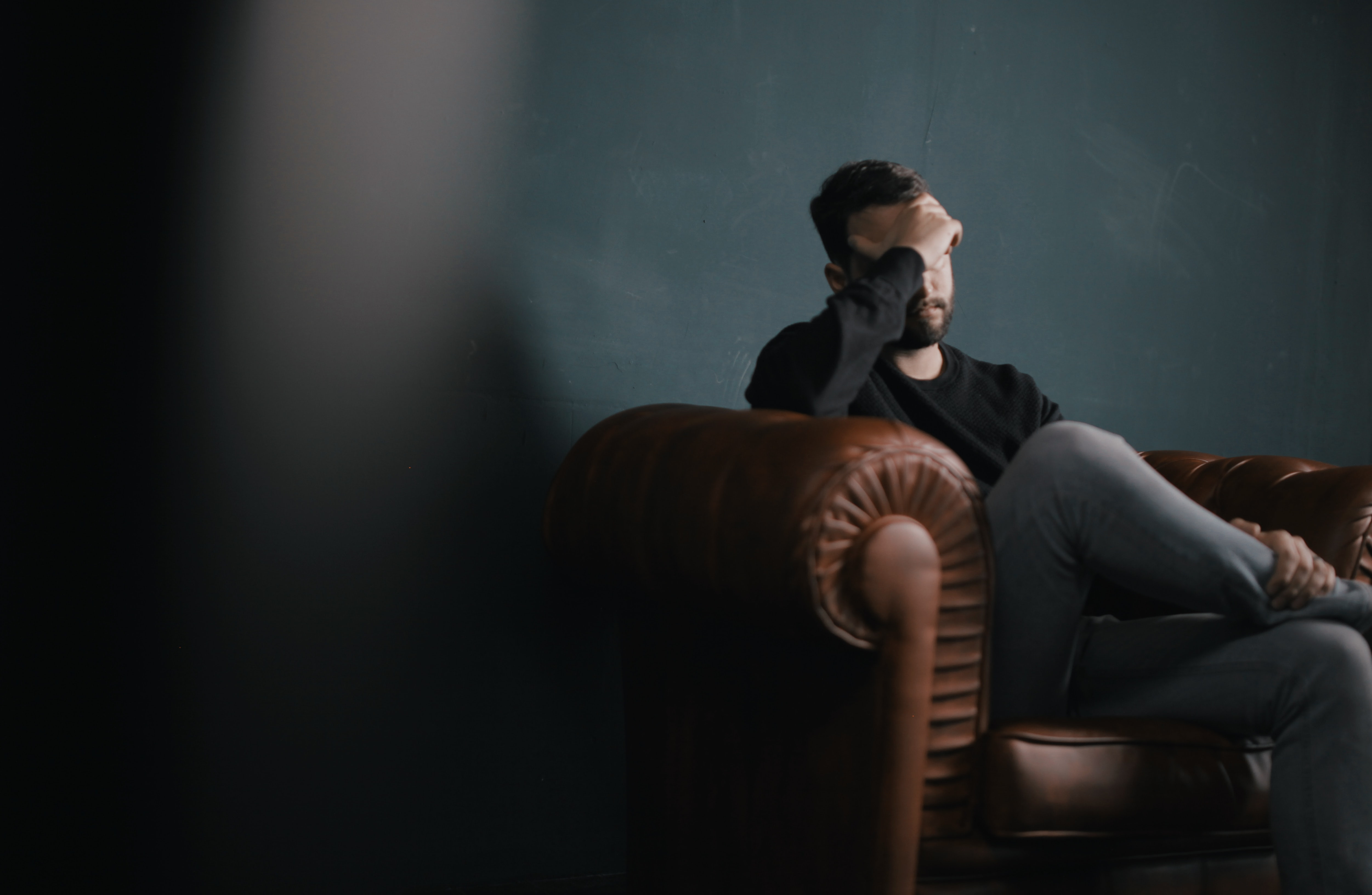 dark picture of a man sat quietly on a sofa with his head in his hands